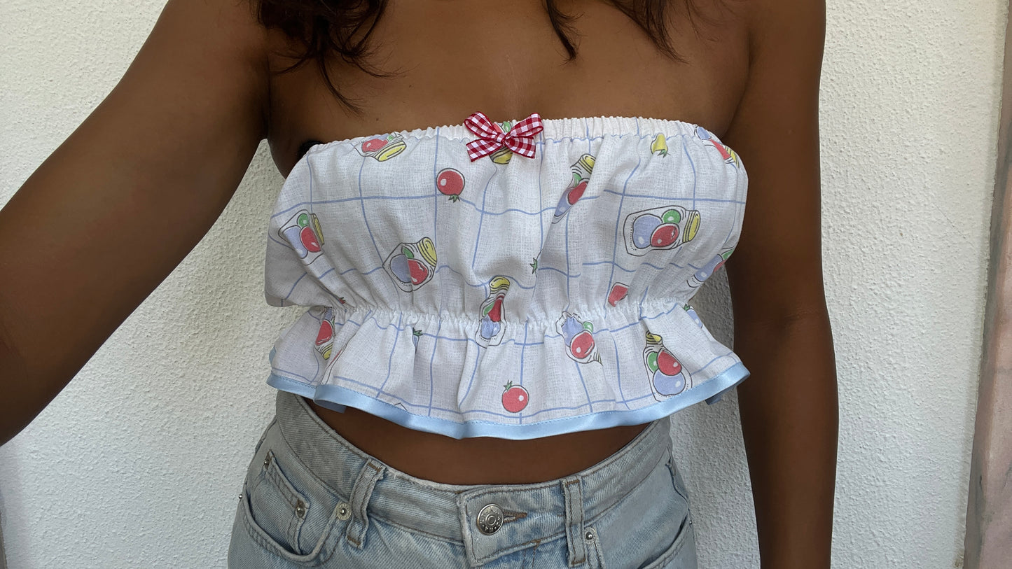 White strapless top with colorful patterns and a bow tie detail, worn by a person against a neutral background.