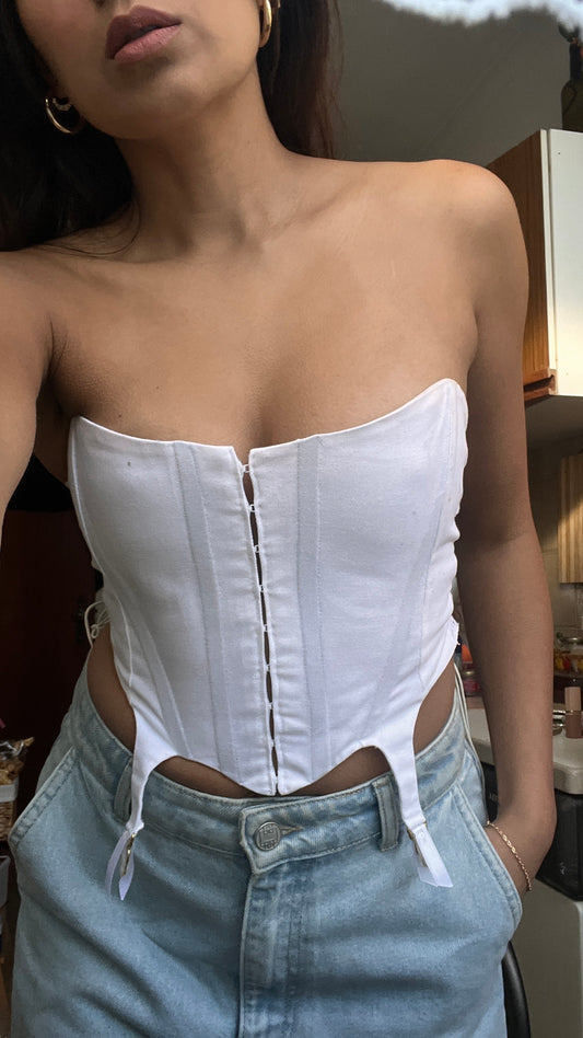 Person wearing a white corset top and light blue jeans indoors.