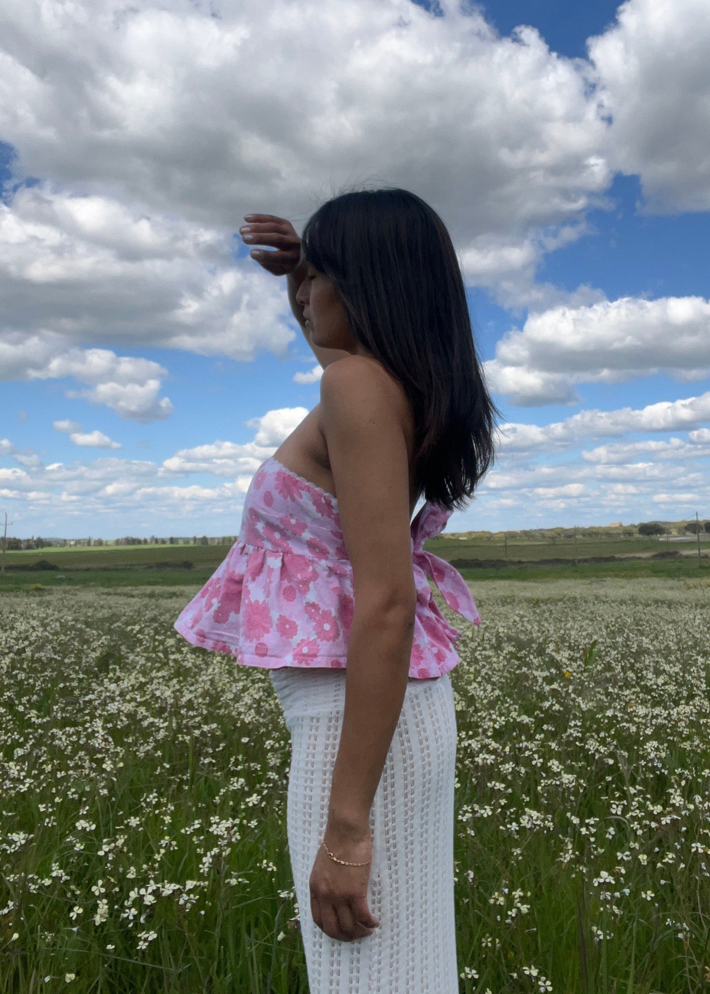 Woman standing in a field with a blue sky and white clouds in the background wearing flower printed top by slow fashion brand Yllin