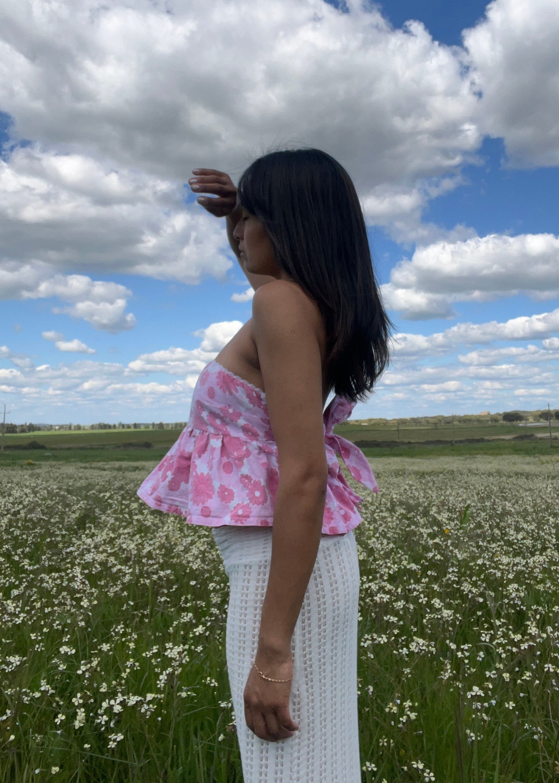 Woman standing in a field with a blue sky and white clouds in the background wearing flower printed top by slow fashion brand Yllin