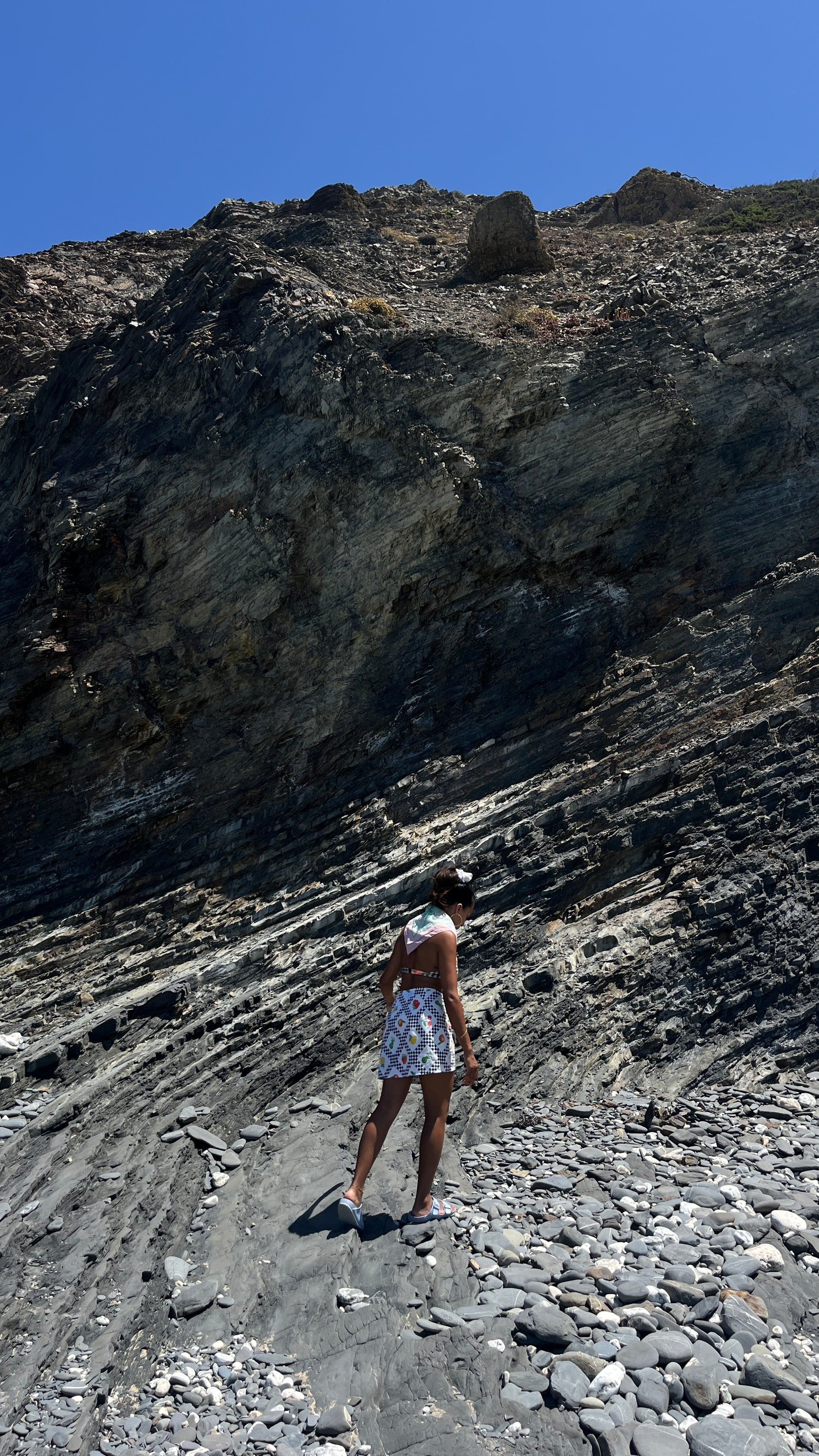 Person standing on a rocky hillside with a clear blue sky