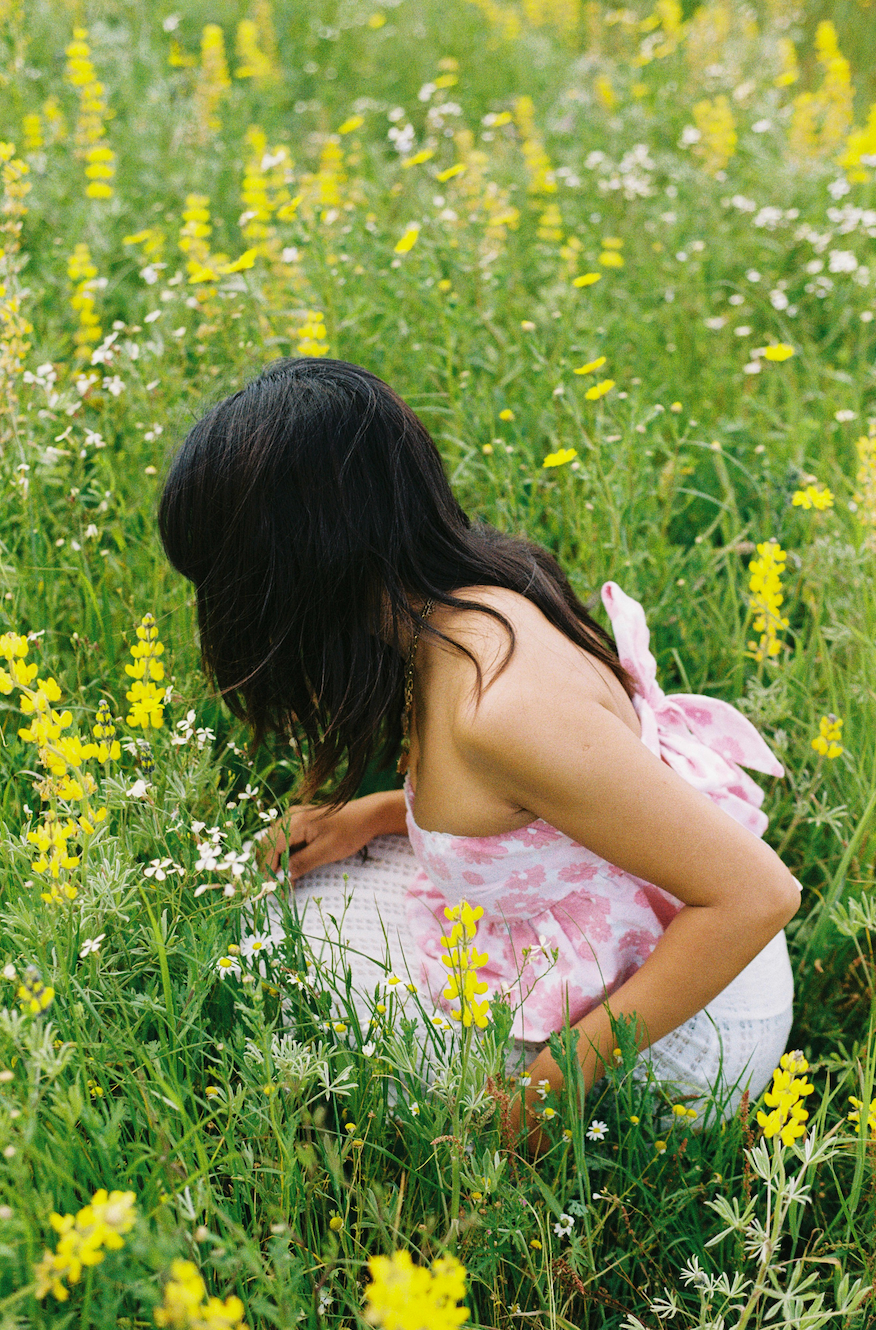 Person wearing a pink floral top sitting a flower field with a patterned top by slow fashion brand Yllin.